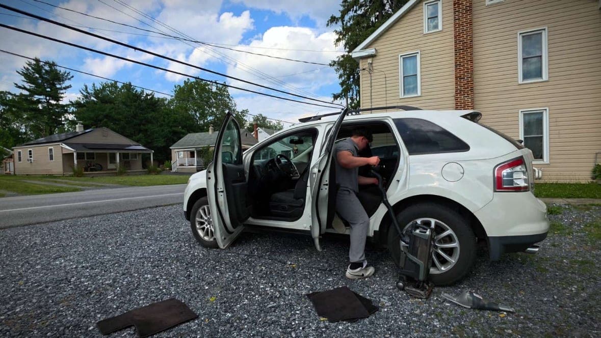 Mike vacuuming the interior of a white Ford Edge with both doors open during a detail